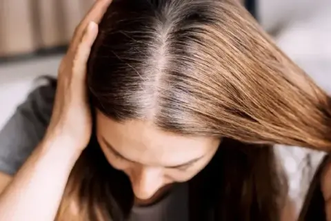 Une femme examine ses racines grasses, cherchant une solution pour sa cure de sebum. Ses mains touchent ses cheveux bruns.