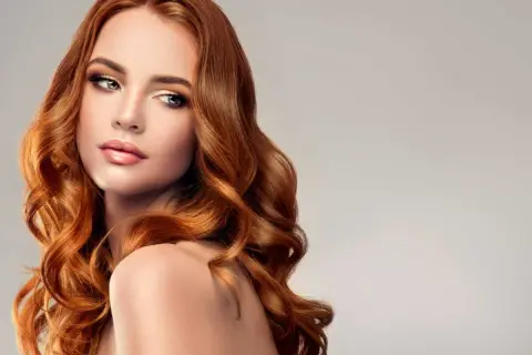 Une femme aux longs cheveux ondulés, d'une magnifique coloration rousse sur brune, pose avec élégance.