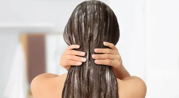 Application d'un masque pour sceller l'hydratation des cheveux. Les mains massent le produit sur les longueurs brunes et humides.