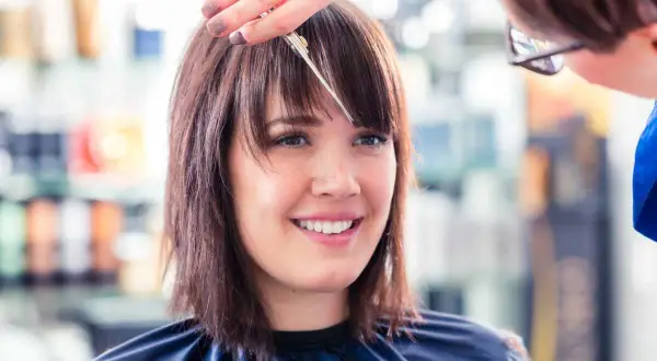 Une coiffeuse ajuste la frange d'une cliente souriante, finalisant une coupe carré.
