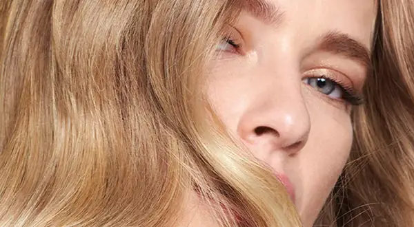 Un gros plan sur le visage d'une jeune femme aux yeux bleus et aux cheveux blond vénitien ondulés, encadrant son visage.