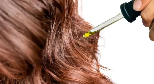 Une goutte d'huile tombe sur des cheveux bruns. Un geste simple pour mettre de l'huile sur les cheveux tous les jours pour les nourrir.