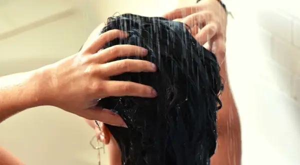 Mains massant des cheveux mouillés sous la douche, comme un soin au beurre de karité cheveux sans rinçage pour une douceur intense.