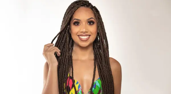 Une femme souriante aux box braids, portant un maillot de bain coloré, joue avec ses tresses.