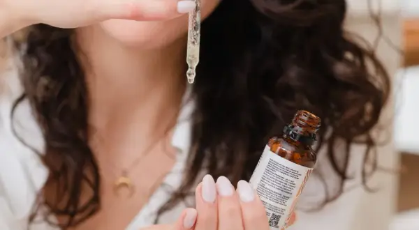 Une femme montre comment appliquer un sérum avec une pipette, une goutte dorée tombant sur sa main.