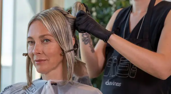 Une coiffeuse applique une couleur ou une mèche pour cacher les cheveux blancs d'une cliente.