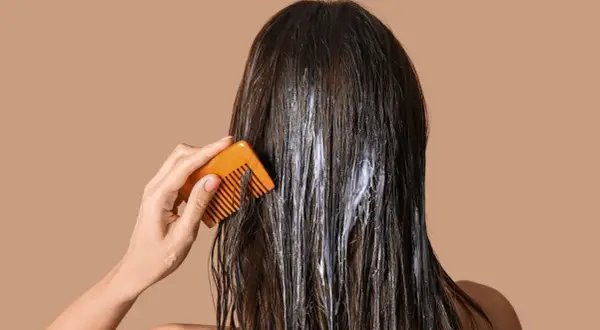 Application d'une coloration végétale sur cheveux. Une main peigne doucement les mèches pour répartir le produit.