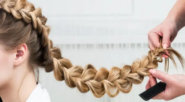 Une main peigne une tresse blonde, une coiffure originale facile à réaliser pour un look sophistiqué.