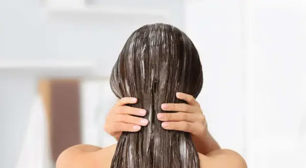 Application d'un soin pour une clarification cheveux. Les mains appliquent le produit sur les longueurs.