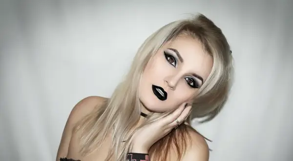Une jeune femme avec une coiffure rock, maquillage intense et lèvres noires. Son regard est captivant.