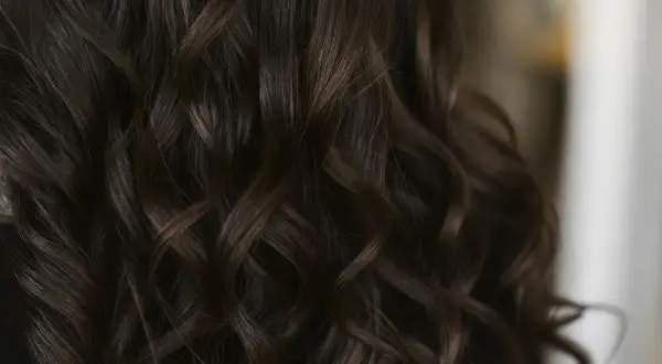 Chevelure brune aux reflets chauds, la couleur gloss cheveux révèle des ondulations soyeuses et lumineuses.