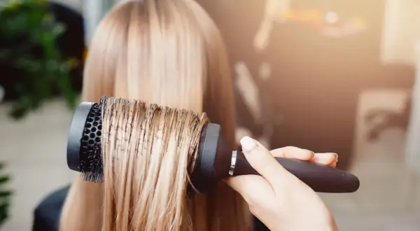 Main d'un coiffeur effectuant un brushing sur des cheveux blonds.