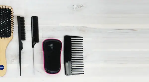 Ensemble de brosses et peignes pour cheveux, dont une brosse à cheveux gras, sur fond de bois clair.