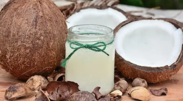 Un pot d'huile de coco, entouré de noix de coco coupées et de coques, un secret naturel pour des cheveux blancs éclatants.