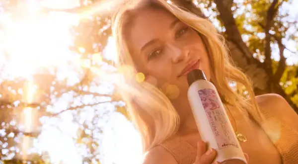 Une femme aux cheveux blonds, avec un balayage naturel, tient un produit Davines sous un soleil éclatant.