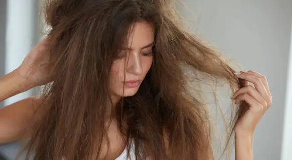 Femme touchant ses cheveux emmêlés, visiblement secs et abîmés, souffrant de cheveux cassants et fourchus.