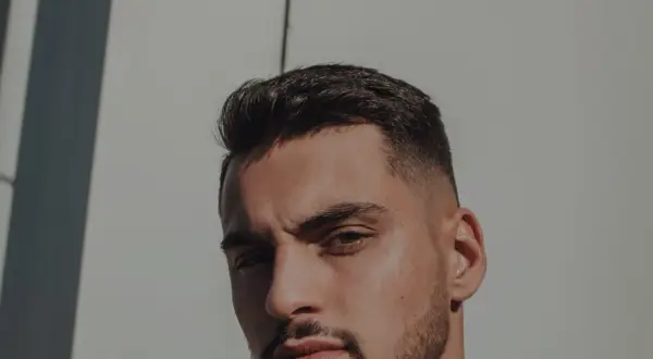 Un homme au chignon homme rasé, regard intense, sous un soleil éclatant.