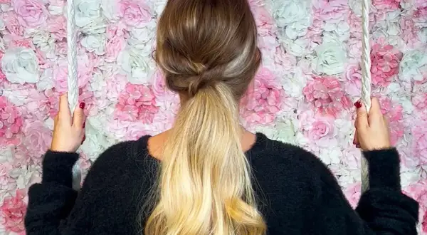 Coiffure semi attachée élégante avec une tresse torsadée, sur fond de mur de fleurs roses et blanches.