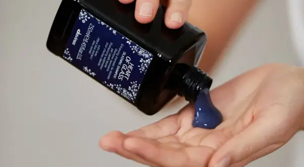 Une main verse un shampoing bleu, idéal pour les cheveux blonds, dans une autre main.