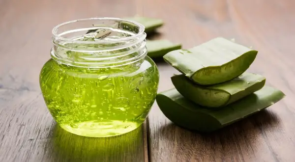 Un pot de gel aloe vera, parfait pour les cheveux, à côté de feuilles d'aloe vera coupées sur fond de bois.