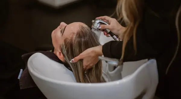 Une femme se fait laver les cheveux dans un salon de coiffure. La question est : combien de fois se laver les cheveux par semaine ?