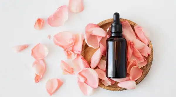 Flacon d'huile essentielle sur un lit de pétales de rose, idéal pour les cheveux gras.