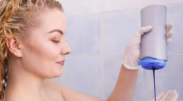 Une femme applique du shampoing violet sur sa main gantée, prête pour un avant-après éclatant.