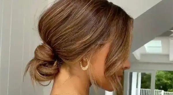 Une coiffure élégante avec un chignon bouclé flou, des mèches encadrant le visage et des boucles d'oreilles dorées.
