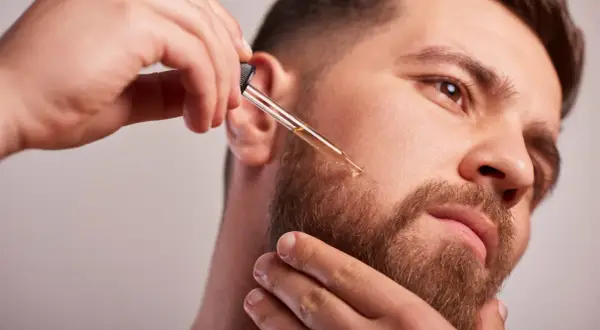 Un homme applique de l'huile de ricin sur sa barbe avec un compte-gouttes pour une pousse plus dense et soyeuse.