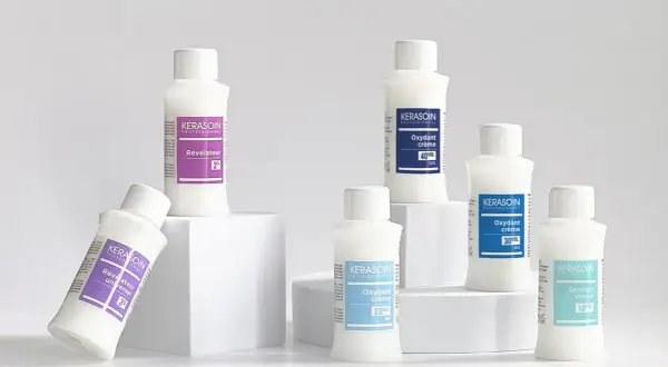 Six bouteilles de produits capillaires Kerasoin, dont un révélateur couleur, disposées sur des cubes blancs.