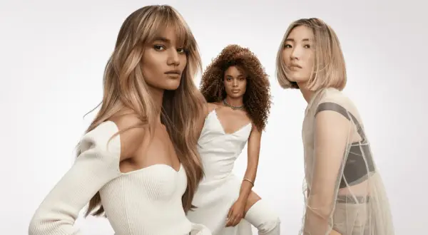 Trois femmes aux coiffures sublimes. La première arbore un french balayage blond, la deuxième des boucles rousses, la troisième un carré blond platine.