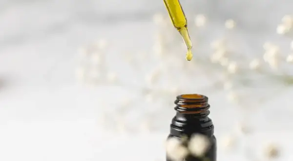 Goutte d'huile de jojoba tombant d'une pipette sur un flacon ambré. Idéal pour des cheveux transformés, avant après.