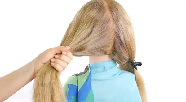 Main d'une femme tenant une mèche de cheveux blonds pour commencer une tresse hollandaise.