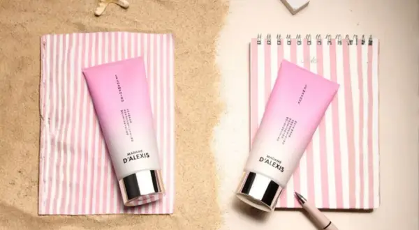 Deux tubes de crème rose sur des serviettes rayées, parfaits pour hydrater les cheveux sec après une journée à la plage.