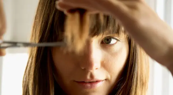 Une femme se coupe les pointes des cheveux. Elle hésite sur combien de cm couper.