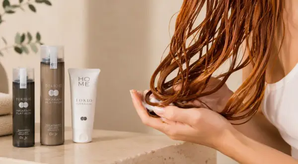 Mains douces appliquant un soin sur des cheveux bouclés roux, avec des produits Tokio Inkarami. Idéal pour la décoloration cheveux bouclés.