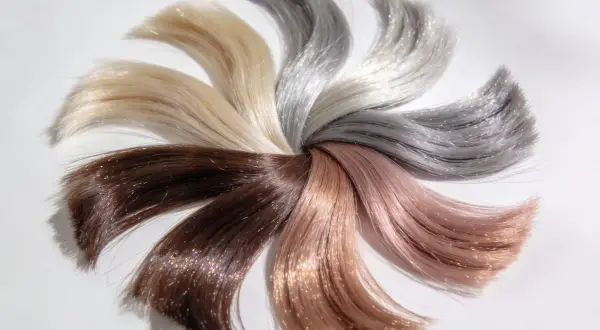 Échantillons de cheveux aux teintes variées, du brun au blond platine, disposés en éventail. Un fond d'éclaircissement subtil met en valeur les reflets chatoyants.