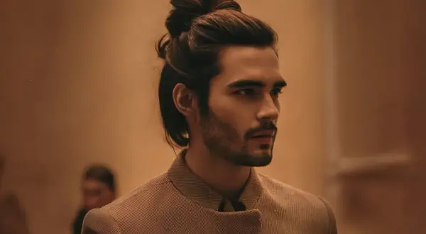 Un homme au chignon homme stylé, portant une veste texturée, regarde au loin.