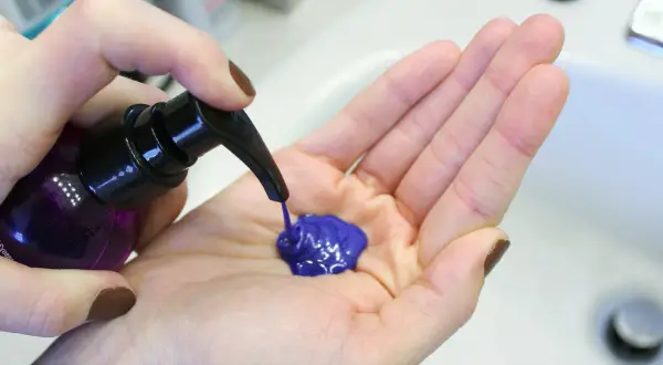 Une main pompe un shampoing bleu vif dans une paume ouverte. Le produit est prêt à être utilisé pour un avant-après spectaculaire.