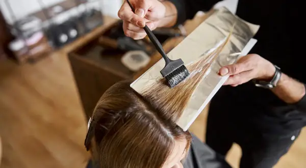 Coiffeur appliquant de la poudre décolorante et oxydant 30 dosage sur des mèches de cheveux, préparant une transformation capillaire.