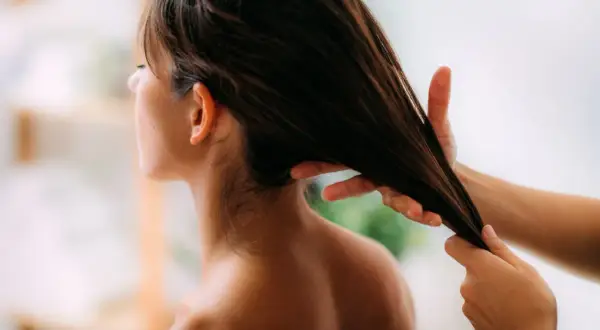 Application d'huile d'olive cheveux pour une brillance naturelle. Une main lisse une mèche de cheveux bruns.