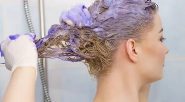 Une femme se lave les cheveux avec du shampoing bleu. Elle porte des gants pour savoir comment enlever le shampoing bleu sur les cheveux.