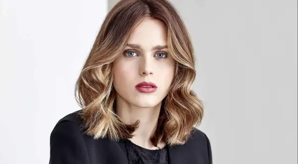 Une femme au regard intense, ses cheveux mi-longs aux reflets blonds et châtains, un parfait exemple de *ombre hair contouring*.
