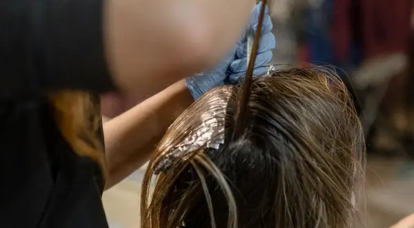 Application d'une patine Dialight sur des mèches de cheveux. Une main gantée applique le produit à l'aide d'un pinceau.