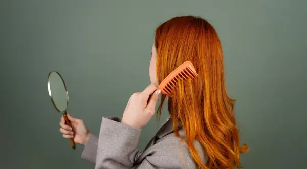 Femme rousse se coiffant, regardant dans un miroir. Elle cherche une solution pour enlever les reflets roux avec du citron.