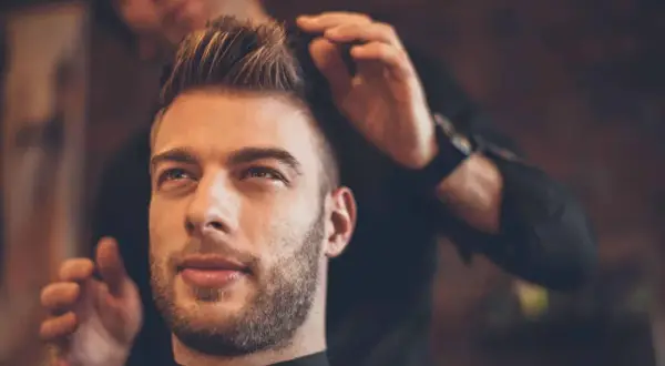 Un homme au regard pensif se fait coiffer une coupe pompadour par un barbier.