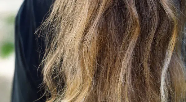 Cheveux longs et ondulés, d'une teinte châtain clair avec des reflets blonds, prêts à teindre ses cheveux en blanc pour un look audacieux.