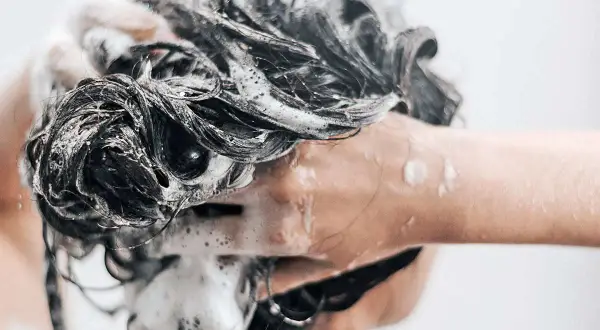 Une main savonne des cheveux sombres et mouillés, créant une mousse abondante. Une question se pose : peut-on se laver les cheveux au savon de Marseille ?