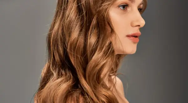 Une femme aux cheveux châtains ondulés, une transformation réussie de blonde à brune, pose de profil.