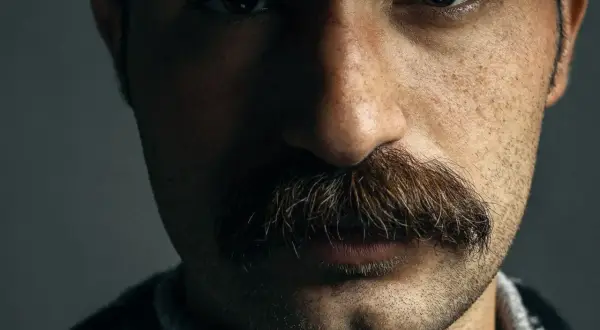 Gros plan sur le visage d'un homme, mettant en valeur un type de moustache broussailleuse et épaisse, aux reflets roux et bruns.